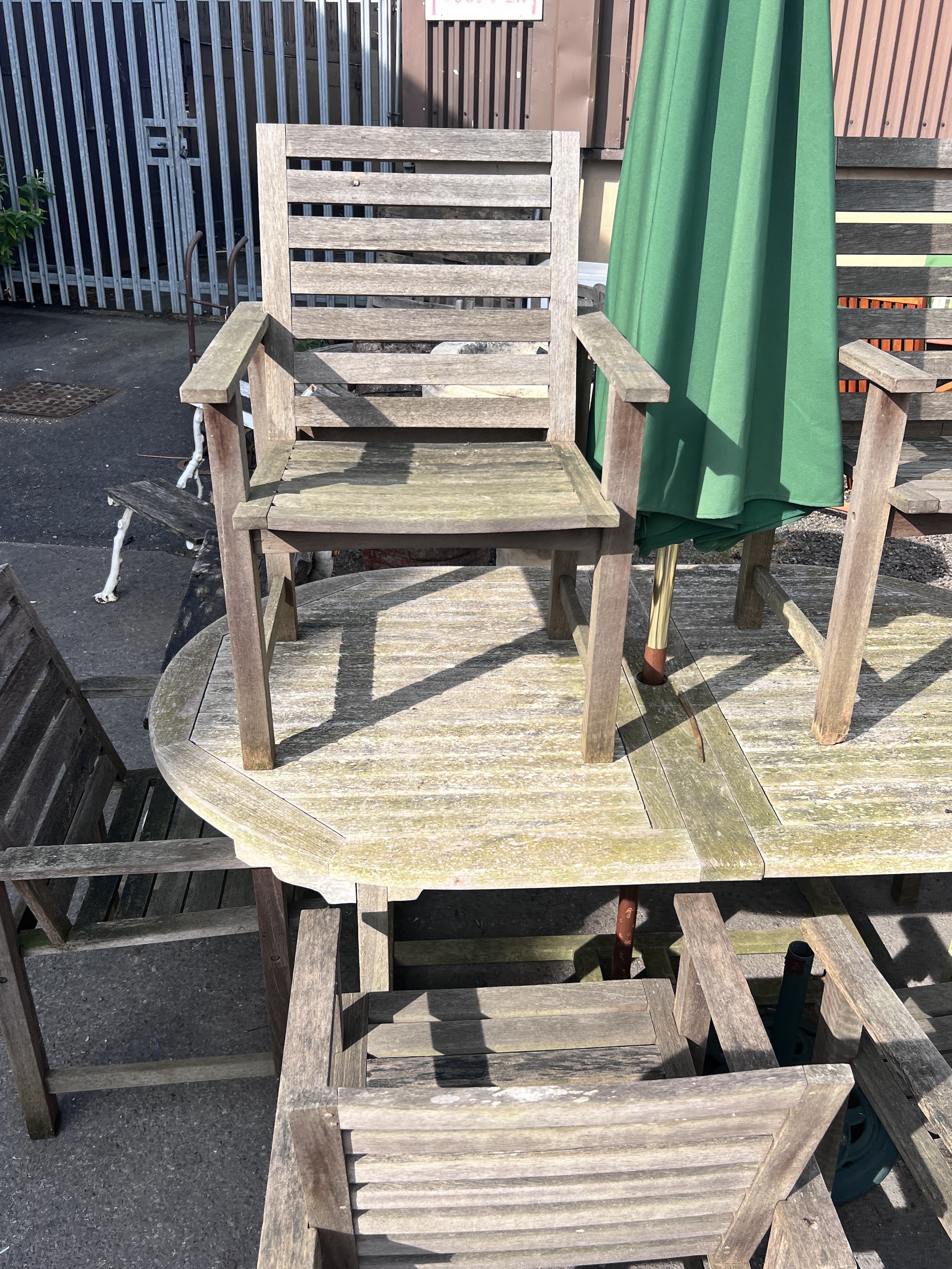A weathered teak extending garden table, length 180cm, depth 110cm, height 76cm, together with six teak garden elbow chairs and a green canvas parasol